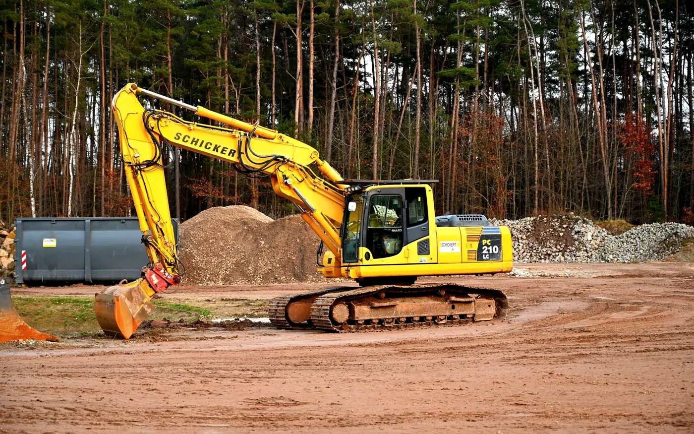 Tracked excavator working a dirt pad at the edge of a woodline
